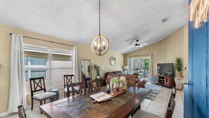 A spacious dining area with a large wooden table, multiple chairs, and a chandelier. There is a television and a plant in the background. - Perfect Getaway-4Bdrm Villa W/Pool in Gated Resort (Kissimmee)