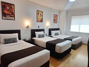 Une chambre d’hôtel avec trois lits, chacun doté d’une tête de lit noire et de draps blancs. Des appliques murales et des œuvres d’art sont disposées au-dessus des lits.
