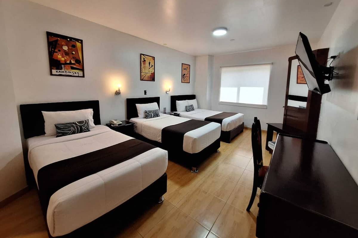 Quarto de hotel com duas camas, uma escrivaninha, uma cadeira e uma televisão.