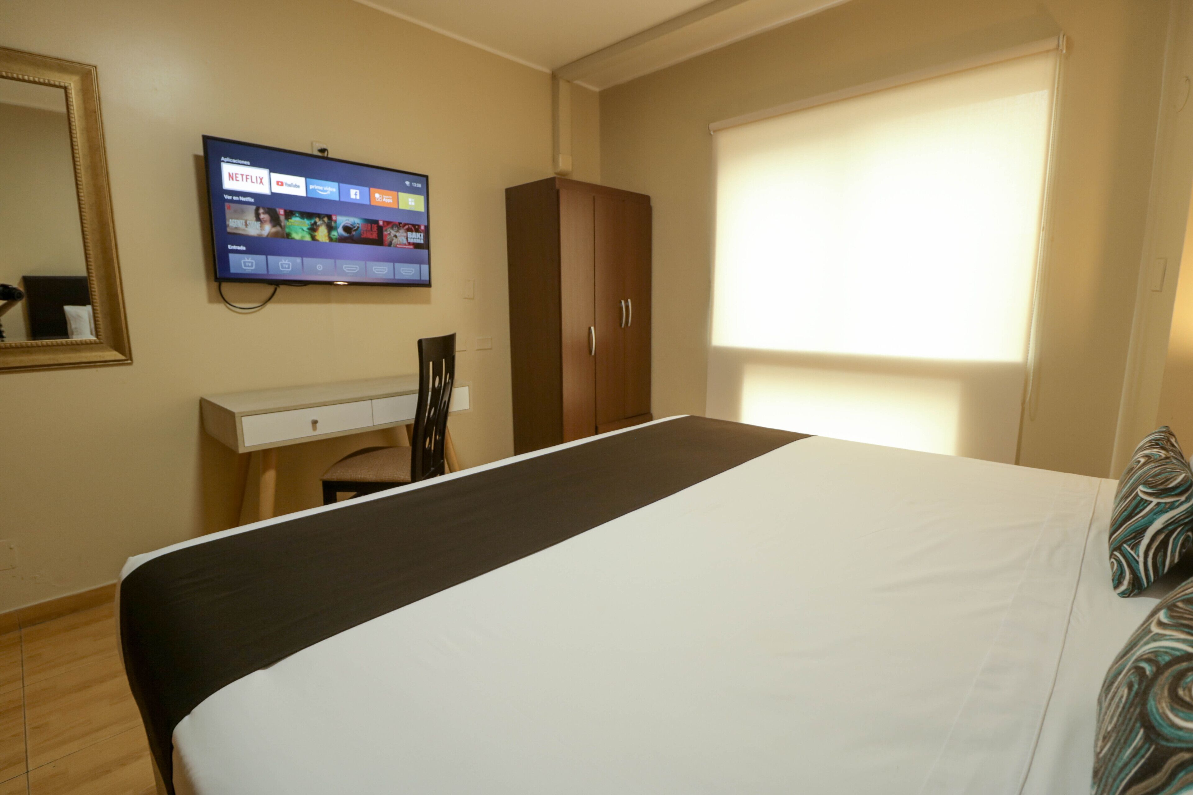 Une chambre d’hôtel équipée d’un lit, d’un bureau, d’une chaise, d’une armoire et d’un téléviseur permettant d’accéder à Netflix.