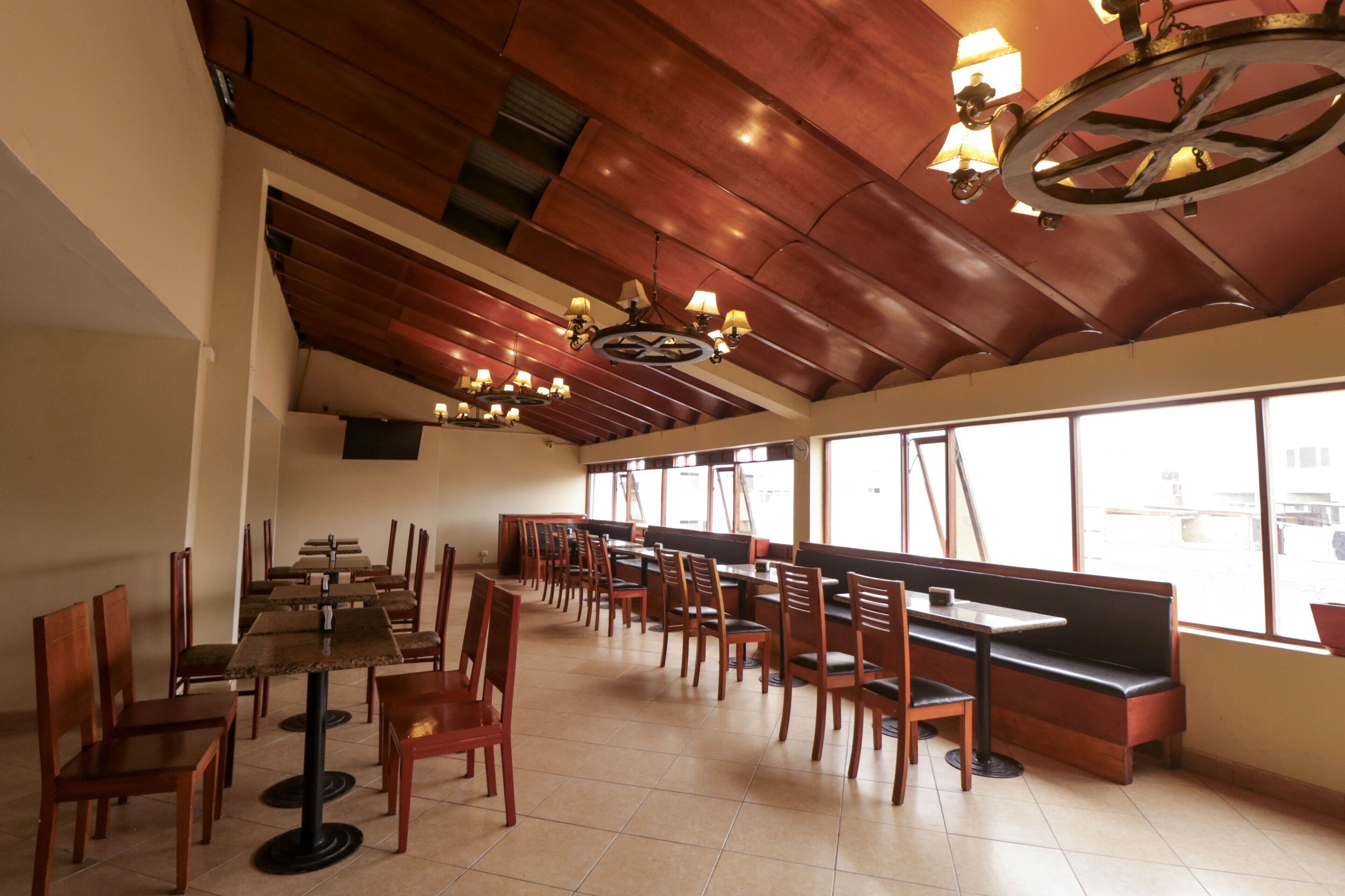 Un restaurante espacioso con mesas y sillas de madera, ventanas amplias y un techo alto con vigas a la vista.