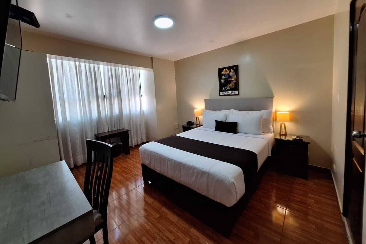 Quarto de hotel com cama, mesas de cabeceira, escrivaninha e cadeira.