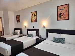 Une chambre d’hôtel avec trois lits, chacun doté d’une tête de lit noire et de draps blancs. Des appliques murales et des œuvres d’art sont disposées au-dessus des lits.