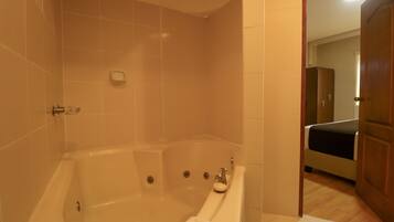 Un baño con bañera, ducha e inodoro. Una puerta de madera da paso a otra habitación.