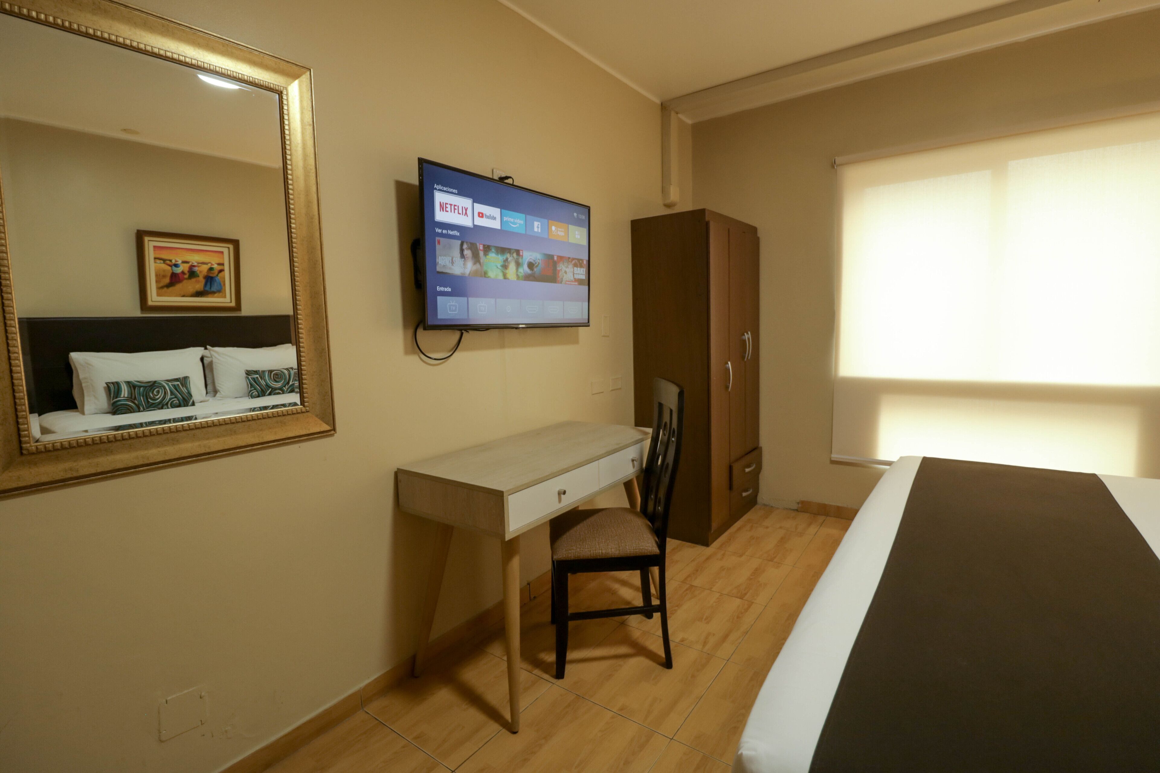 A hotel room with a bed, a desk, a chair, a television mounted on the wall, and a wardrobe.