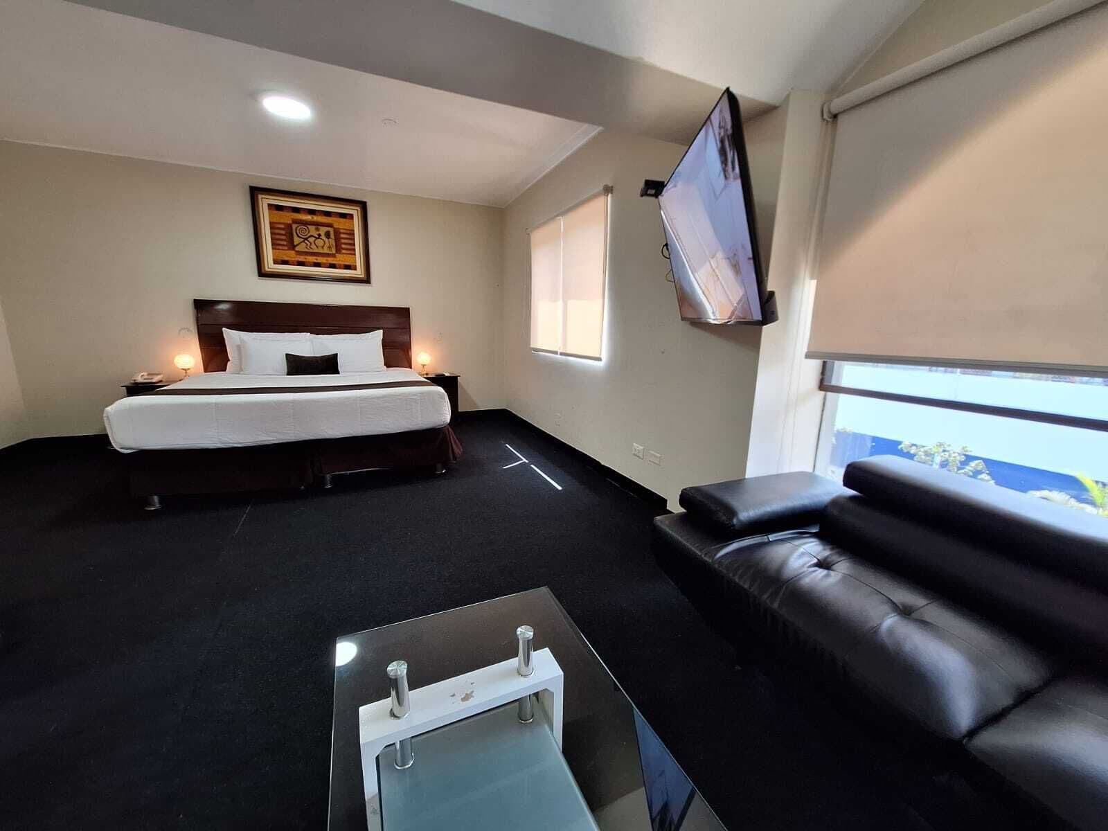 A hotel room with a bed, a sofa, a TV, and a window.