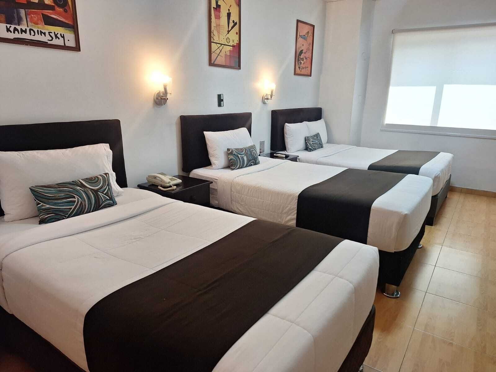 A hotel room with three beds, a nightstand with a phone, wall-mounted lights, and artwork.