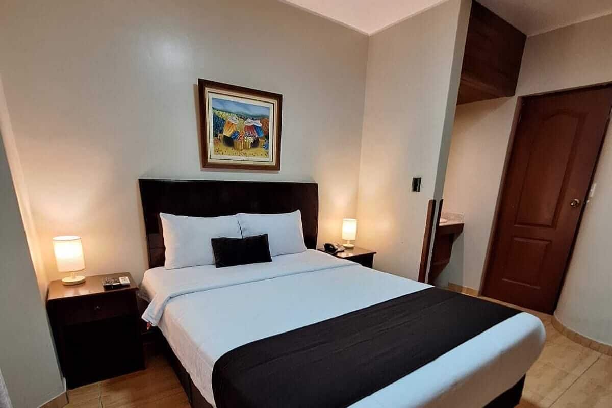 A hotel room with a large bed, two bedside tables with lamps, a wooden floor, a door, and a painting on the wall.
