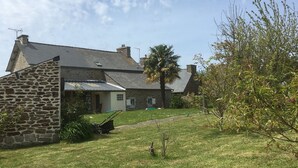 Een stenen huis met een schuin dak, een kleine tuin en een palmboom.