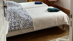 Een kamer met een bed, een raam met gordijnen, houten wanden en een klein plankje met decoratieve spullen.