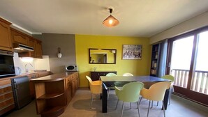 Eine moderne Küche mit Holzausstattung, einem Essbereich mit Tisch und Stühlen, einem großen Fenster und einer Deckenleuchte.