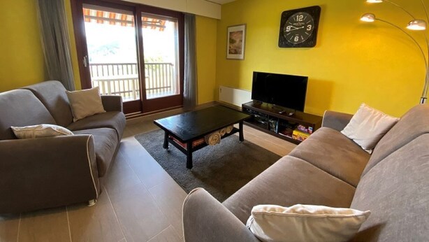 Ein Wohnzimmer mit einer Couch, einem Couchtisch, einem Fernseher und einem Balkon.