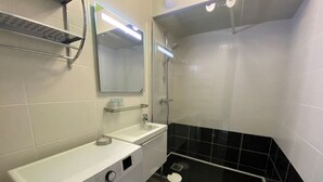 Ein modernes Badezimmer mit Waschmaschine, Waschbecken, Spiegel und Duschbereich.