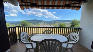 Ein Balkon mit Tisch und Stühlen, Blick auf eine Stadt und Berge, und ein Streifenmarkise.