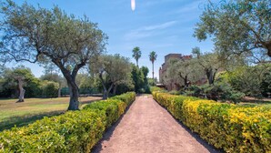 Un sentier bordé de haies et d’arbres soigneusement taillés, qui mène à un bâtiment à la façade rouge.