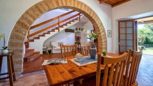 Un espace repas comprenant une table en bois, des chaises et un arc qui mène à un escalier.