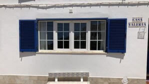 A building with a white facade, blue shutters, and a tiled bench outside.