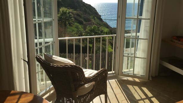 A balcony with a wicker chair, a view of the ocean, and a wooden fence.