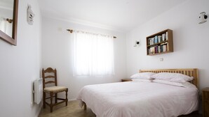A bedroom with a bed, a chair, a bookshelf, and a window with curtains.