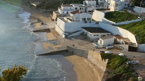 A coastal village with white buildings, a beach, and a rocky hillside.