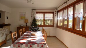A dining room with a long table, chairs, a Christmas tree, and a window with curtains. - LA COURTIONE APARTMENT IN CHALET (Samoëns)