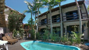 Piscina con muelle de madera, sillones de descanso y plantas tropicales.