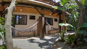 Un edificio de madera con una hamaca, un banco y un jardín con rocas y plantas.