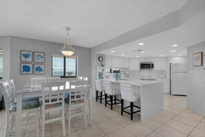 Une cuisine moderne avec des meubles blancs, un îlot central et un coin repas comprenant des chaises blanches et une table en verre.