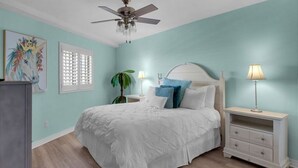 Un dormitorio con cama, mesitas de noche, ventilador de techo y ventana con persianas.
