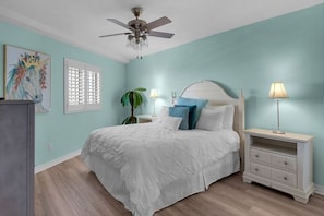 Une chambre à coucher avec un lit, des tables de chevet, un ventilateur de plafond et une fenêtre avec des stores.