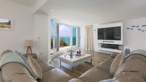 Una sala de estar moderna con un televisor grande, una mesa de centro de vidrio y un sofá.