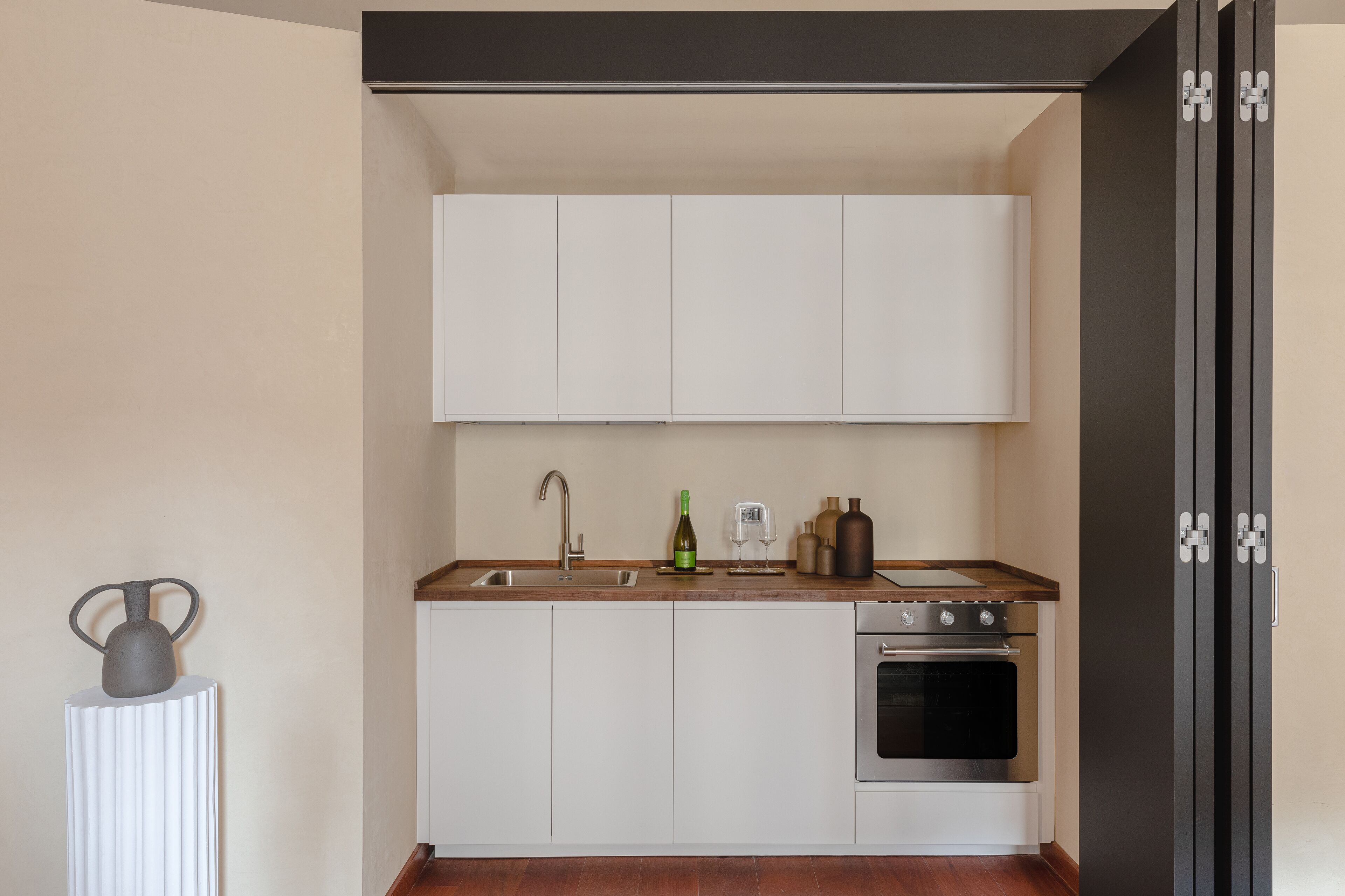 A compact kitchen with white cabinets, a stainless steel oven, and a wooden countertop.
