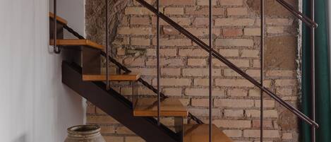 Una escalera con un muro de ladrillo de fondo, una columna blanca y un jarrón sobre la columna.