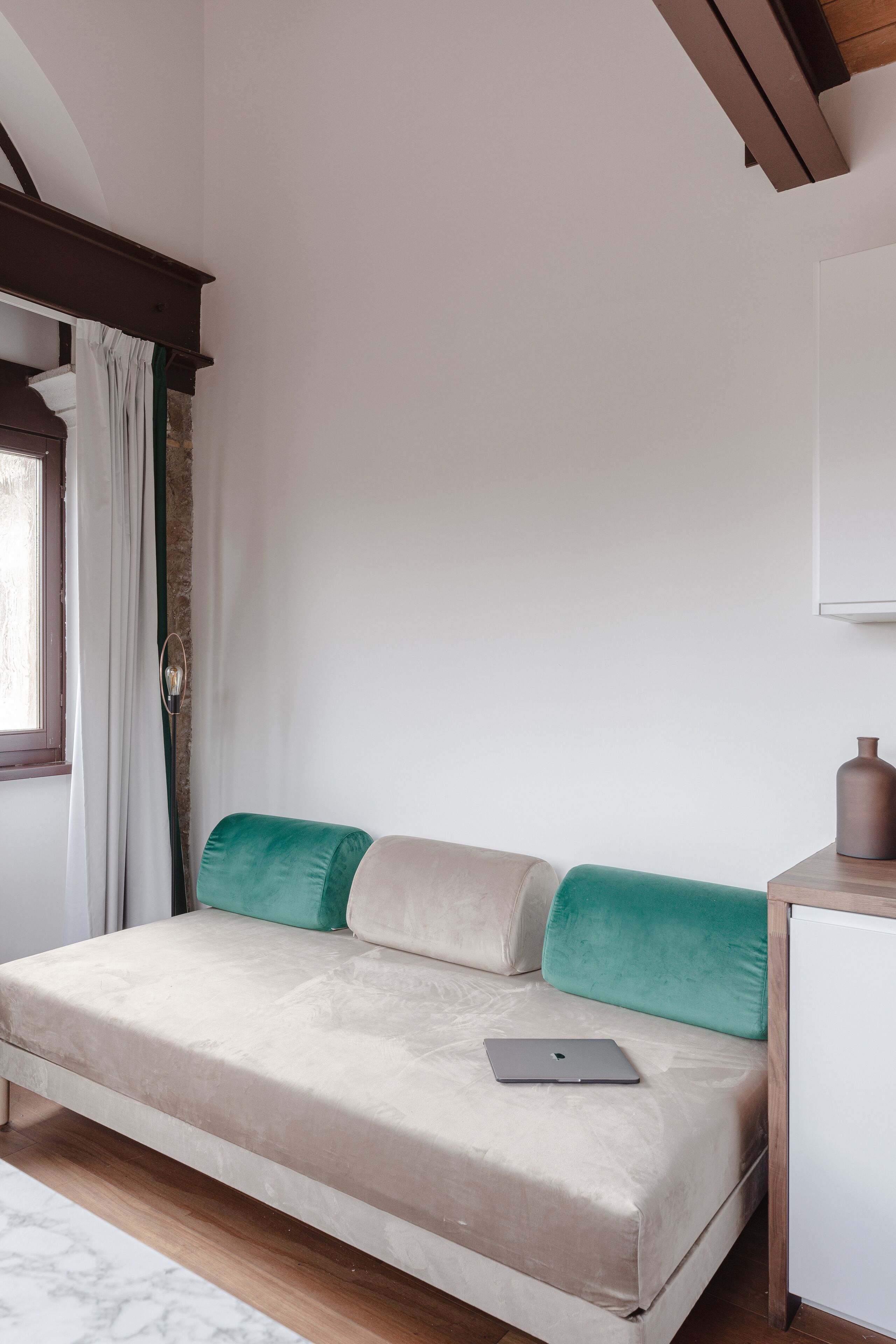 A bedroom with a bed, a laptop, a nightstand, and a window with curtains.