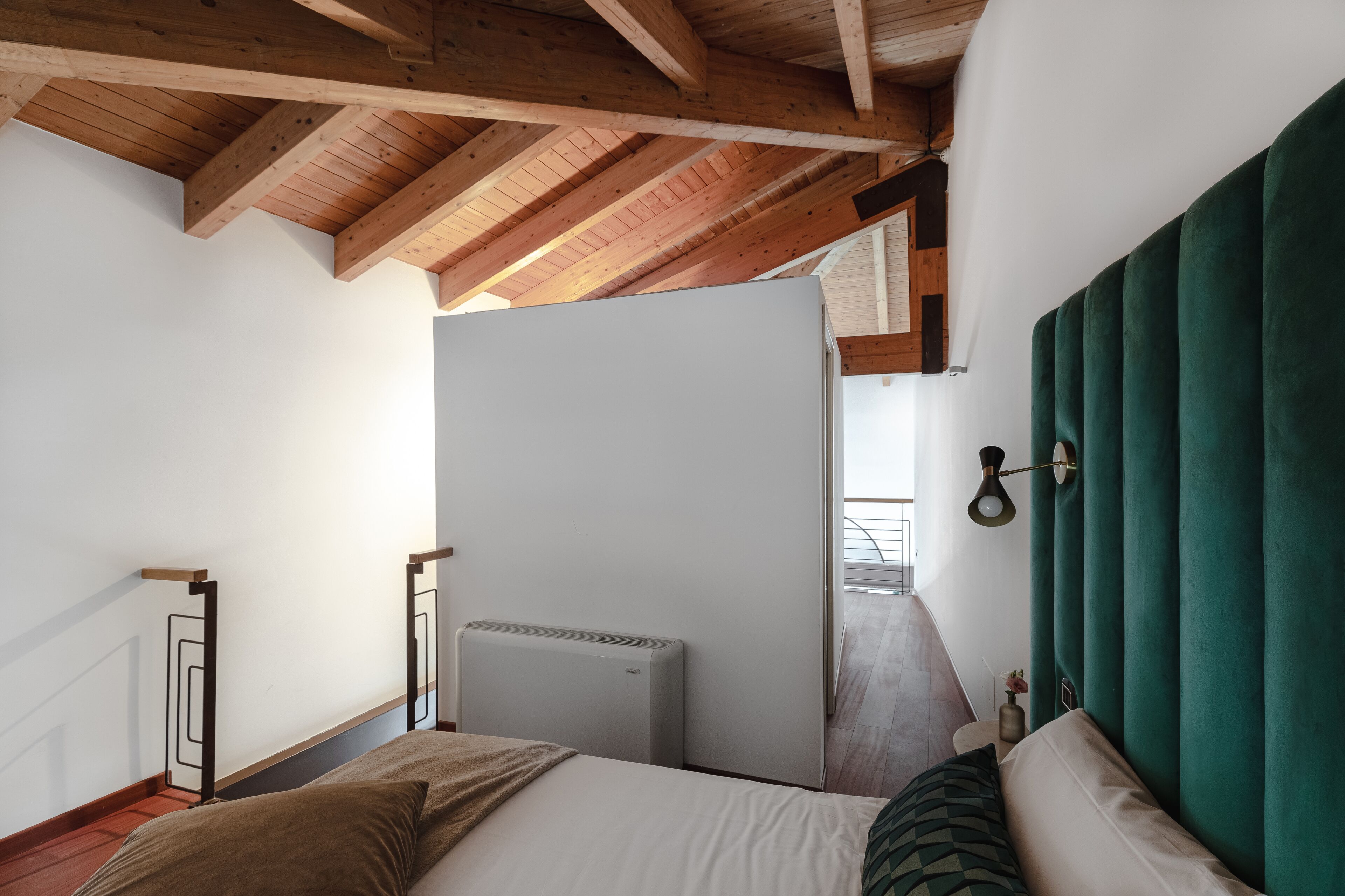 Un dormitorio con techo de madera, una cama con cabecera verde y un radiador.