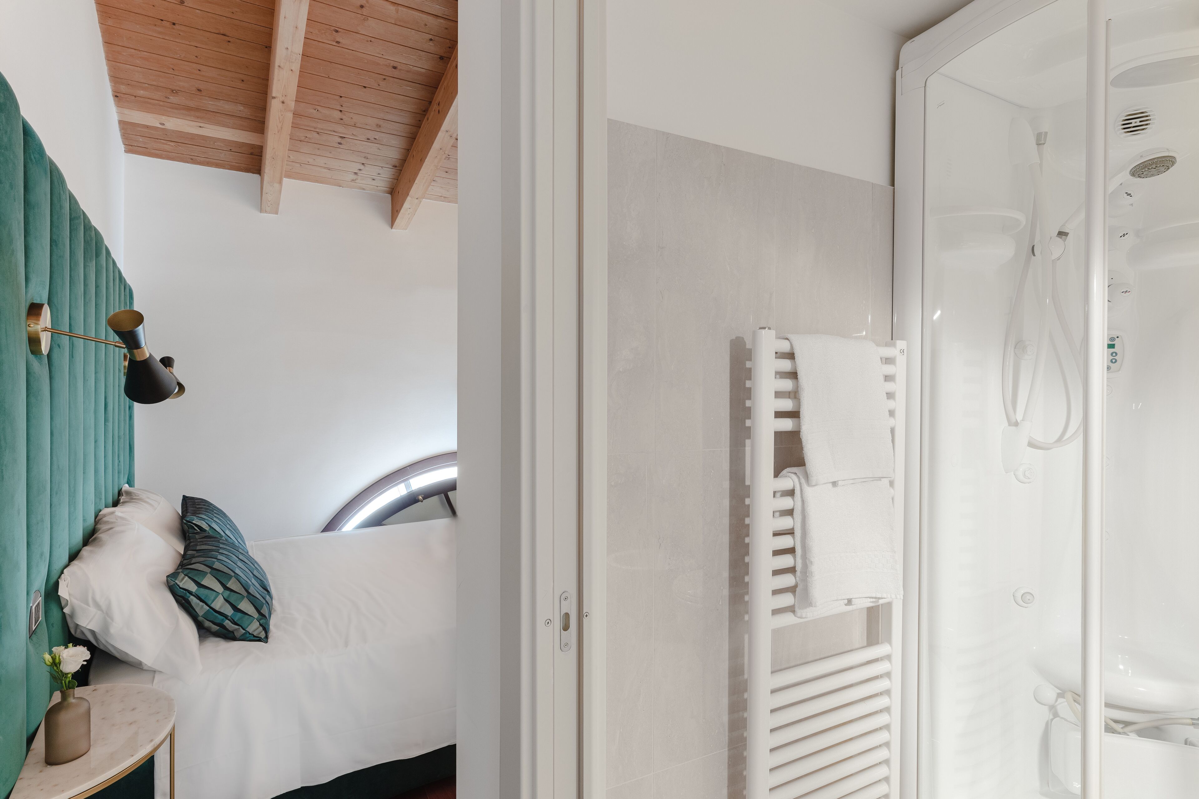 A bathroom with a shower, a towel rack, and a bed with a green headboard.