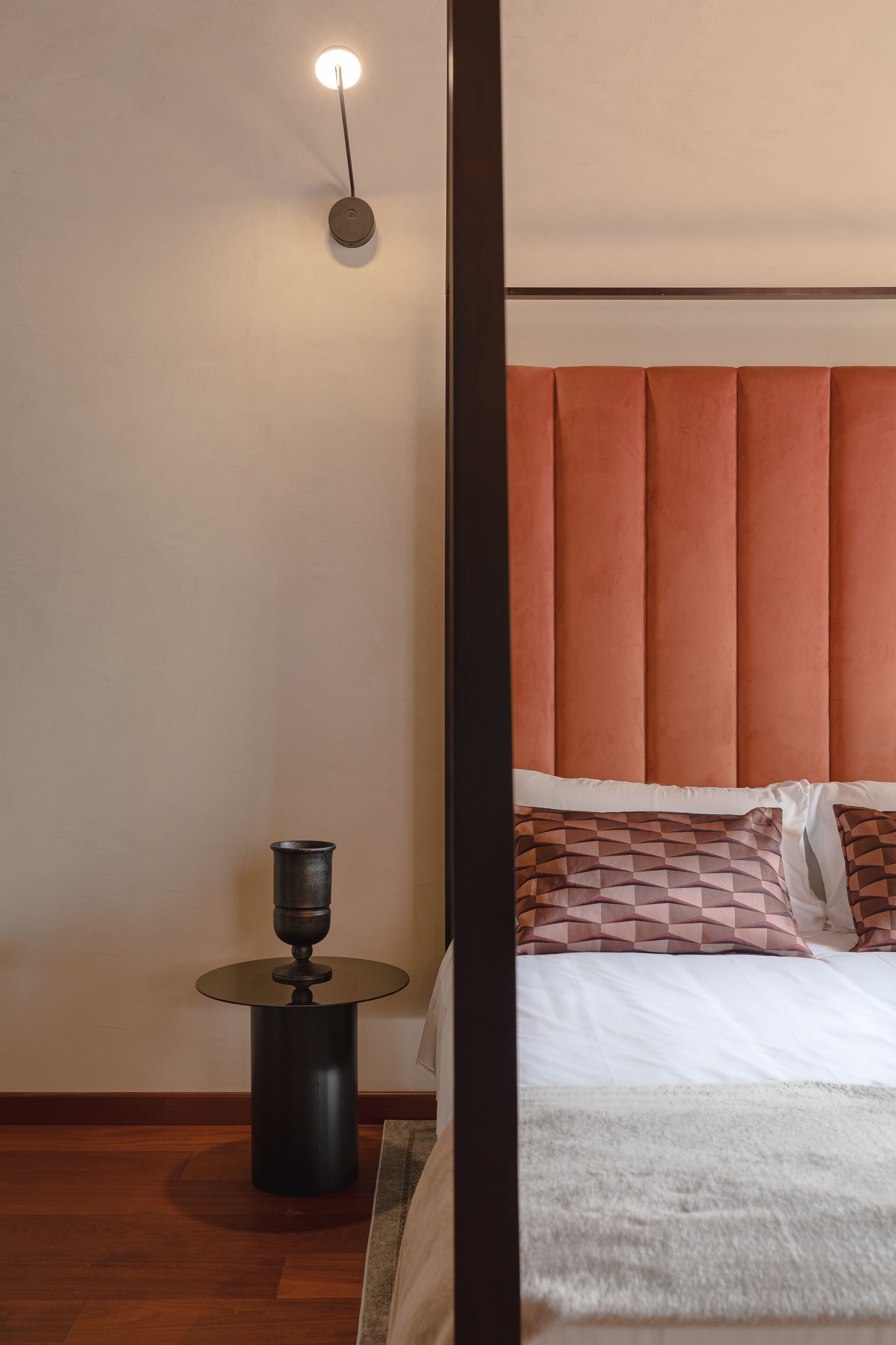 A bedroom with a bed, a nightstand, a lamp, and a wall-mounted light fixture.