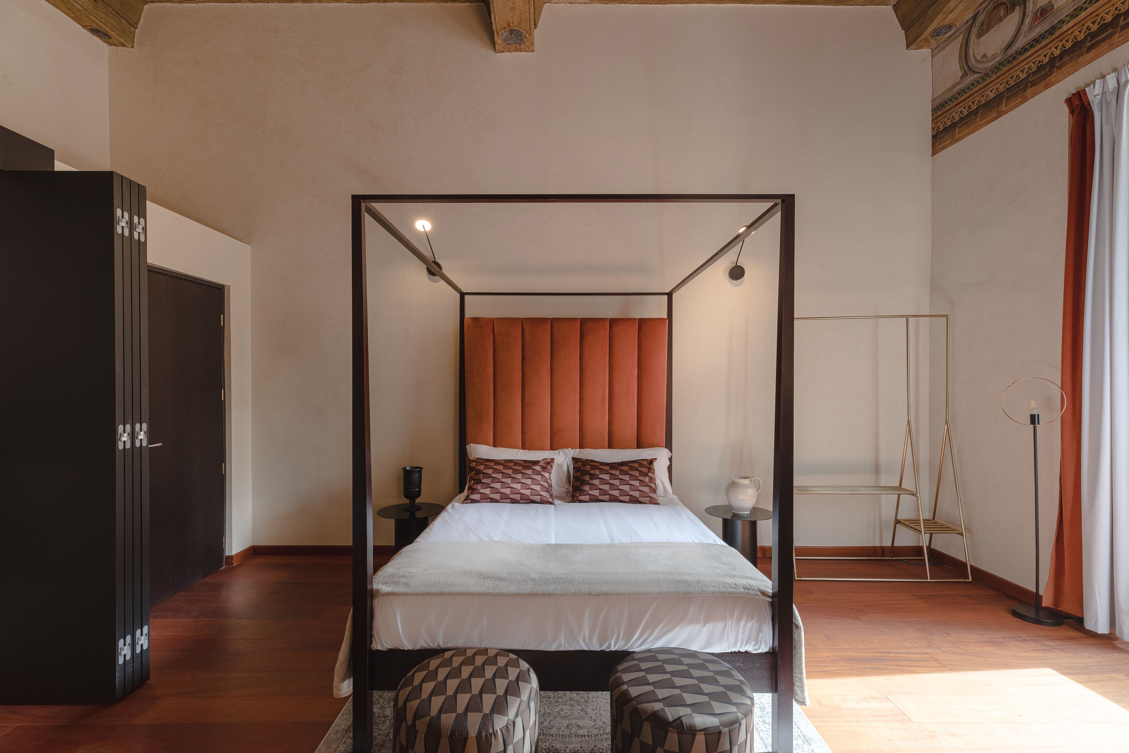 Una cama con dosel, un cabecero de madera, dos mesitas de noche y una lámpara de pie.