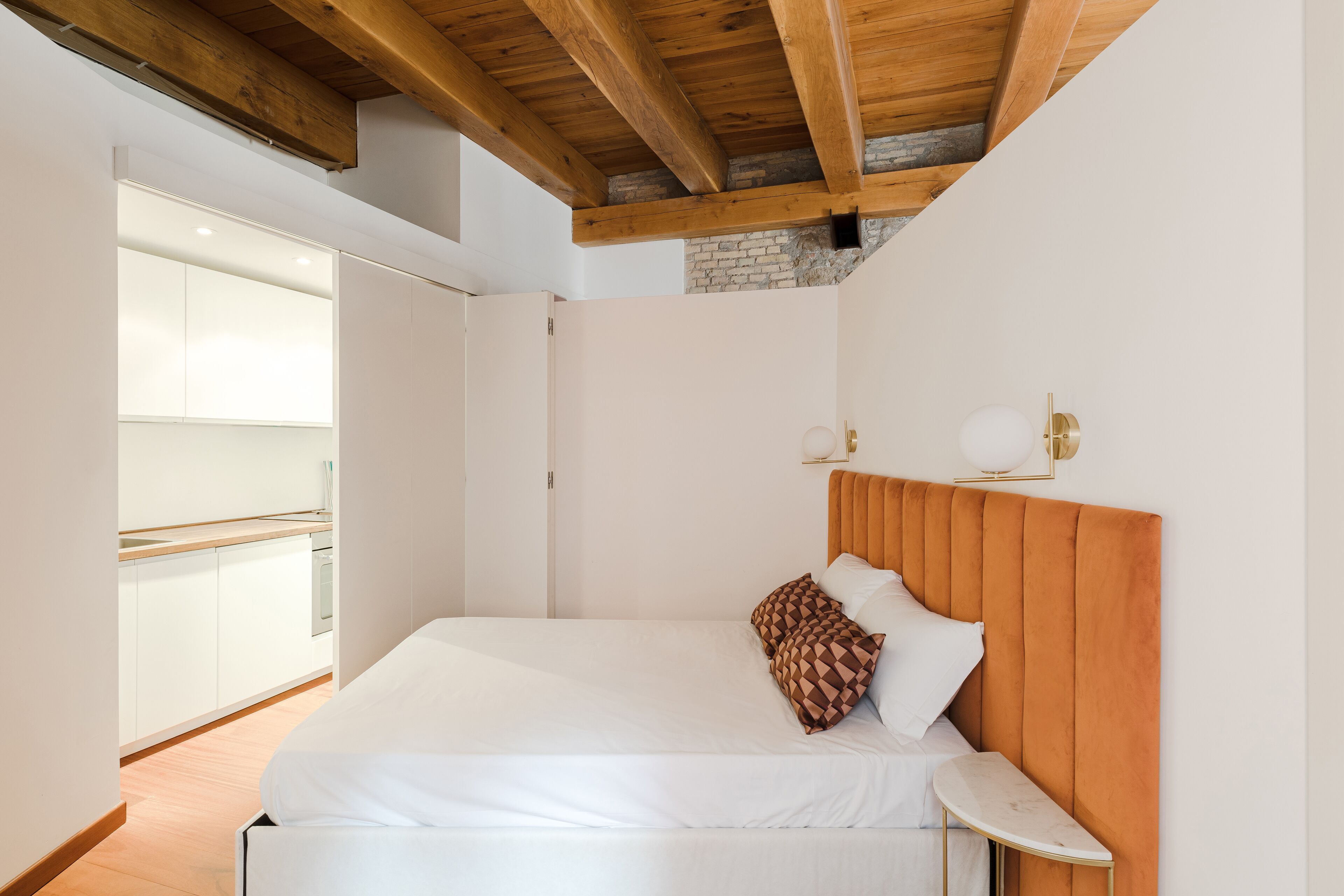 Un dormitorio moderno con techo de madera, una cama blanca y vistas a una zona de cocina.