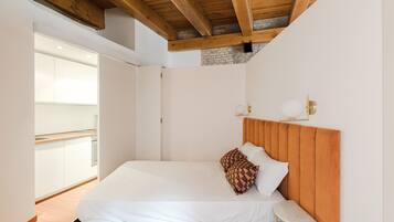 Un dormitorio moderno con techo de madera, una cama blanca y vistas a una zona de cocina.