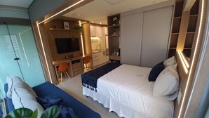 A modern hotel room with a large bed, a desk, and a kitchenette.