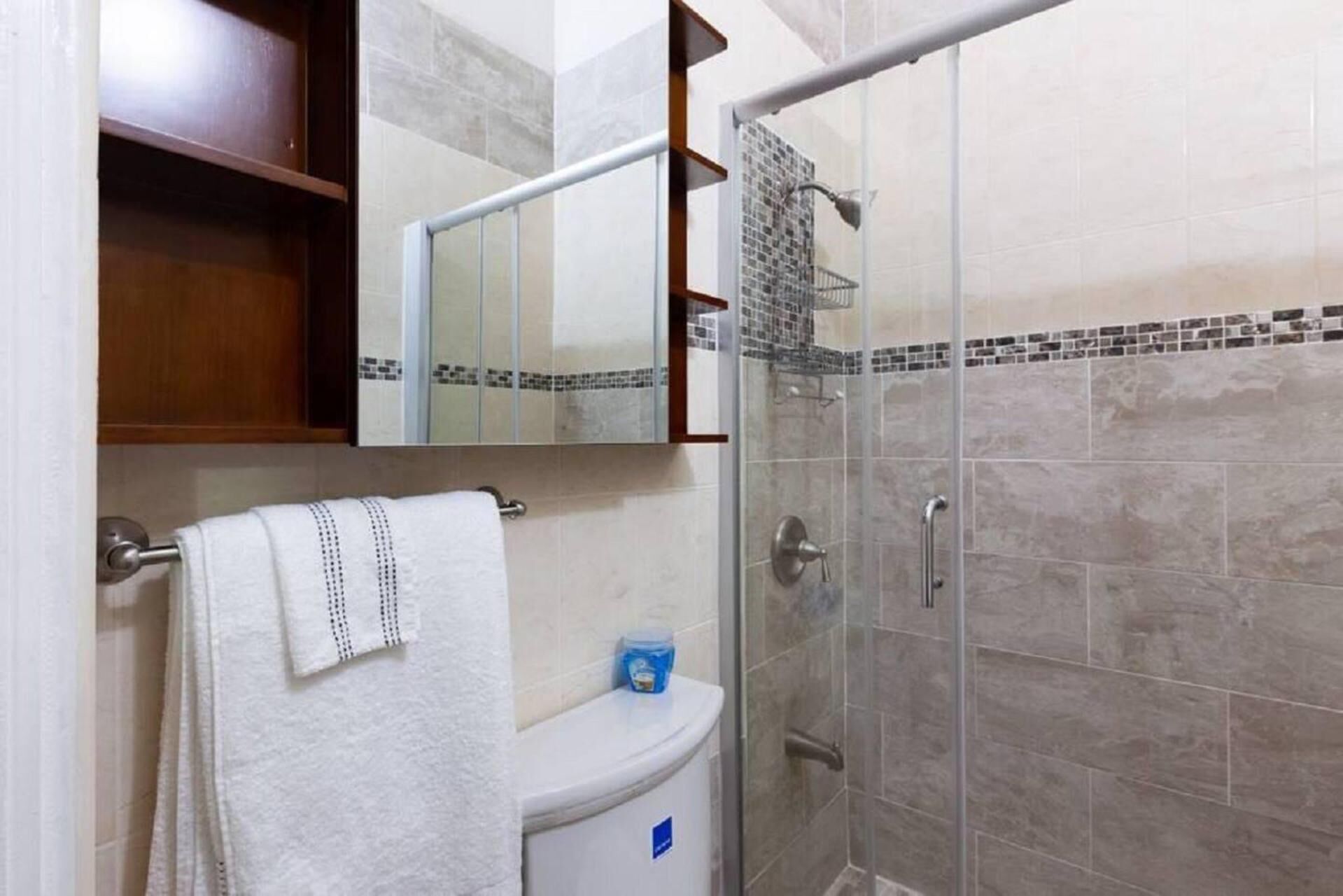 Une salle de bain comprenant des toilettes, un porte-serviettes, une cabine de douche en verre et un mur carrelé.