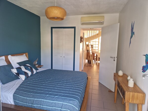Een slaapkamer met een bed, een garderobe, een hanglamp en uitzicht op een andere kamer.