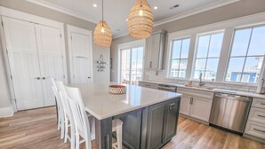 A modern kitchen with a large island, white cabinetry, and a view to the outside. - Gorgeous water views, a private swimming pool & easy access to private beach! (Cape Charles)