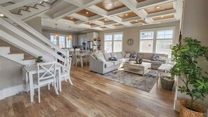 A spacious living area with a staircase, wooden flooring, and a modern kitchen in the background. - Gorgeous water views, a private swimming pool & easy access to private beach! (Cape Charles)