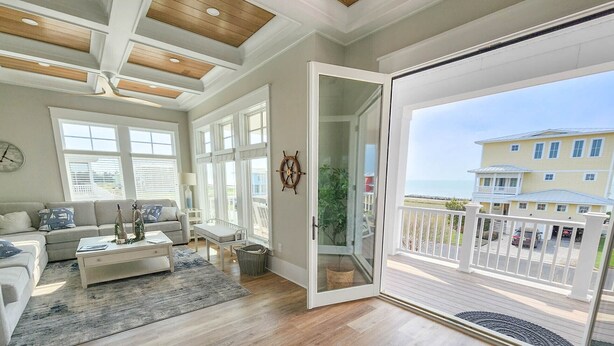 A spacious living room with a large sliding glass door leading to a balcony, wooden flooring, and a view of a residential area. - Gorgeous water views, a private swimming pool & easy access to private beach! (Cape Charles)