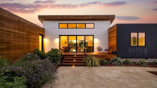 A modern two-story house with a concrete driveway, wooden and dark siding, and a well-lit entrance. - Year-Round Heated Pool | Hot Tub | Fire Pit | Huge Lawn | Vineyard Views (Kenwood)
