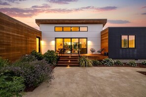 Una casa moderna de dos pisos con entrada bien iluminada, camino de hormigón y revestimiento de madera oscura.