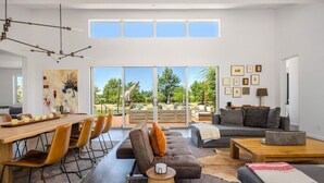 A modern living room with a dining area, large windows, and a view of the outdoors. - Year-Round Heated Pool | Hot Tub | Fire Pit | Huge Lawn | Vineyard Views (Kenwood)