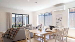 Un salon moderne avec un canapé, une table à manger et des chaises. Une grande fenêtre offre une vue sur l’extérieur.